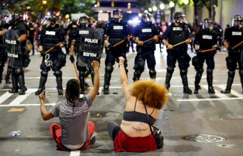 Two people sit on the ground as they protest in front of police in uptown Charlotte, NC  during a protest of the police shooting of Keith Scott, in Charlotte, North Carolina, U.S. September 21, 2016. REUTERS/Jason Miczek