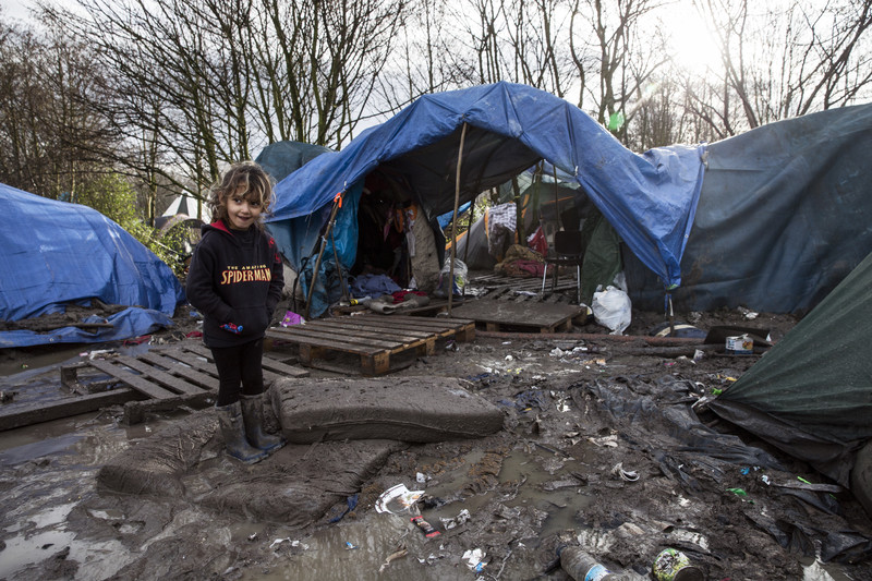 epa05097442 A Kurdish child stands over a drenched mattress half sinked in the mud next to her family tent in the makeshift migrant camp in Grande-Synthe near Dunkerque, France, 11 January 2016. Despite most of the attention is on the so-called 'Jungle' in near-by Calais, the refugee camp in Grande-Synthe counts an estimated 3,000 residents. A decision to relocate the refugee camp inhabitans to a new to-be-constructed building, aimed to improve miserable conditions, is expected to be made.  EPA/ETIENNE LAURENT